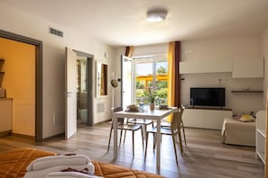 Ein Hotelzimmer mit Bett, Essbereich mit Tisch und Stühlen, Fernseher und einem Fenster mit Vorhängen.