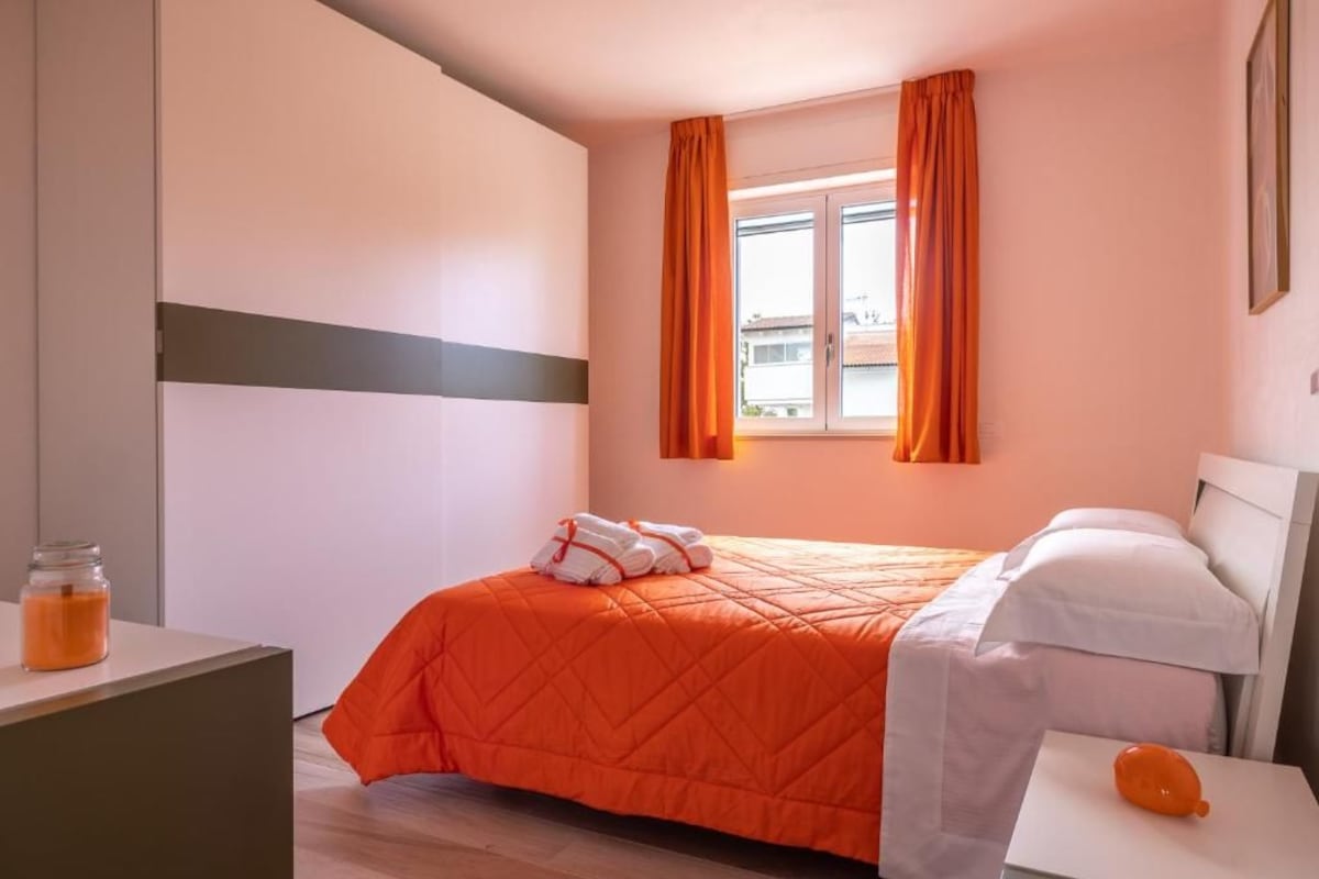 Ein Hotelzimmer mit Bett, Nachttisch, einem Fenster mit Vorhängen und einer Wandlampe.