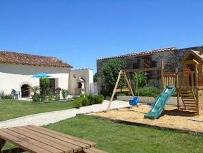 A patio with a wooden table, a children's play area with a slide, and a stone building with a tiled roof. - Holiday Home 'Limerac, Cottage' with Shared Pool, Shared Terrace and Wi-Fi (Salles-Lavalette)