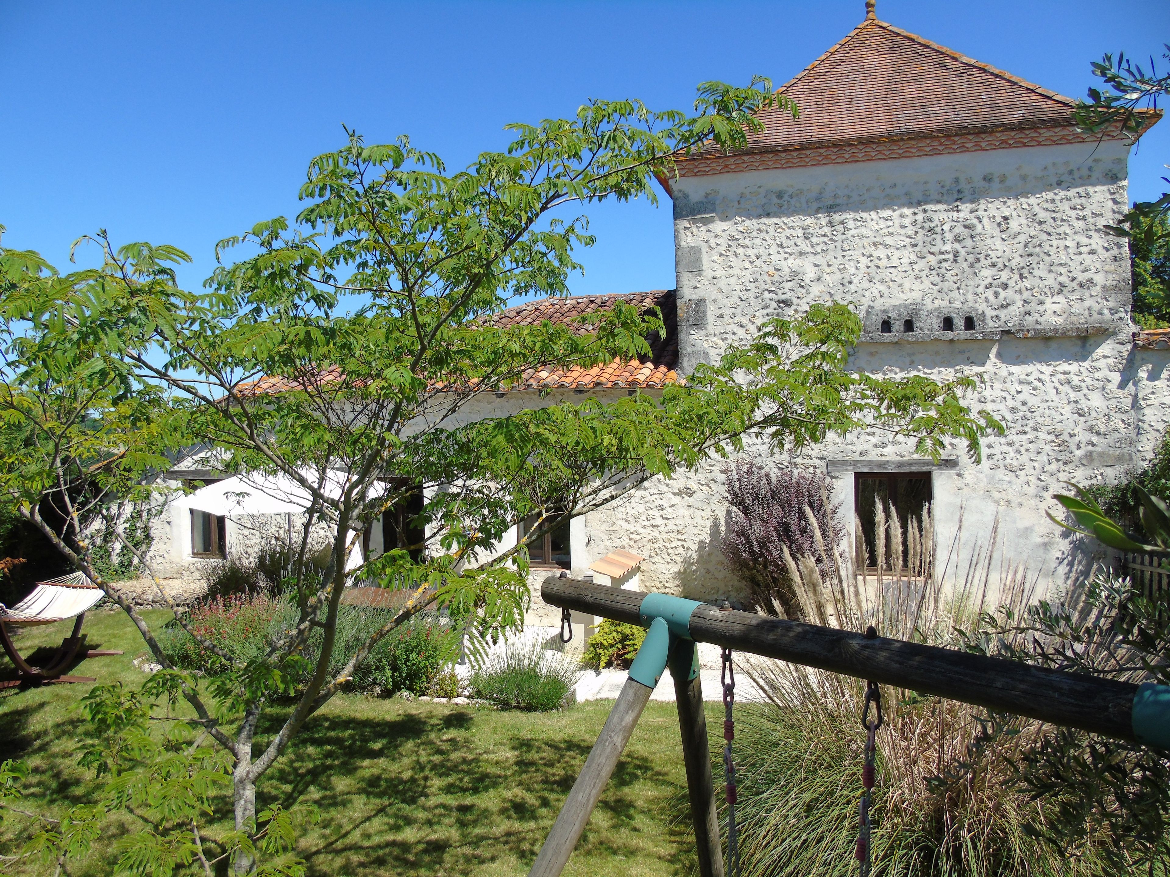 A stone building with a tiled roof, surrounded by greenery and a hammock.