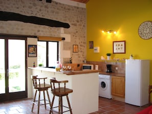 A kitchen with a washing machine, a refrigerator, and a bar area with stools. - Holiday Home 'Limerac Farmhouse' with Shared Pool, Shared Terrace and Wi-Fi (Salles-Lavalette)