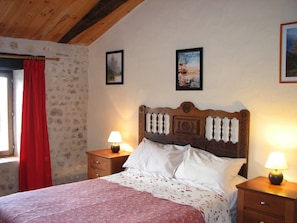 A bedroom with a wooden headboard, two bedside tables with lamps, a bed with white linens, and a window with a red curtain. - Holiday Home 'Limerac Farmhouse' with Shared Pool, Shared Terrace and Wi-Fi (Salles-Lavalette)