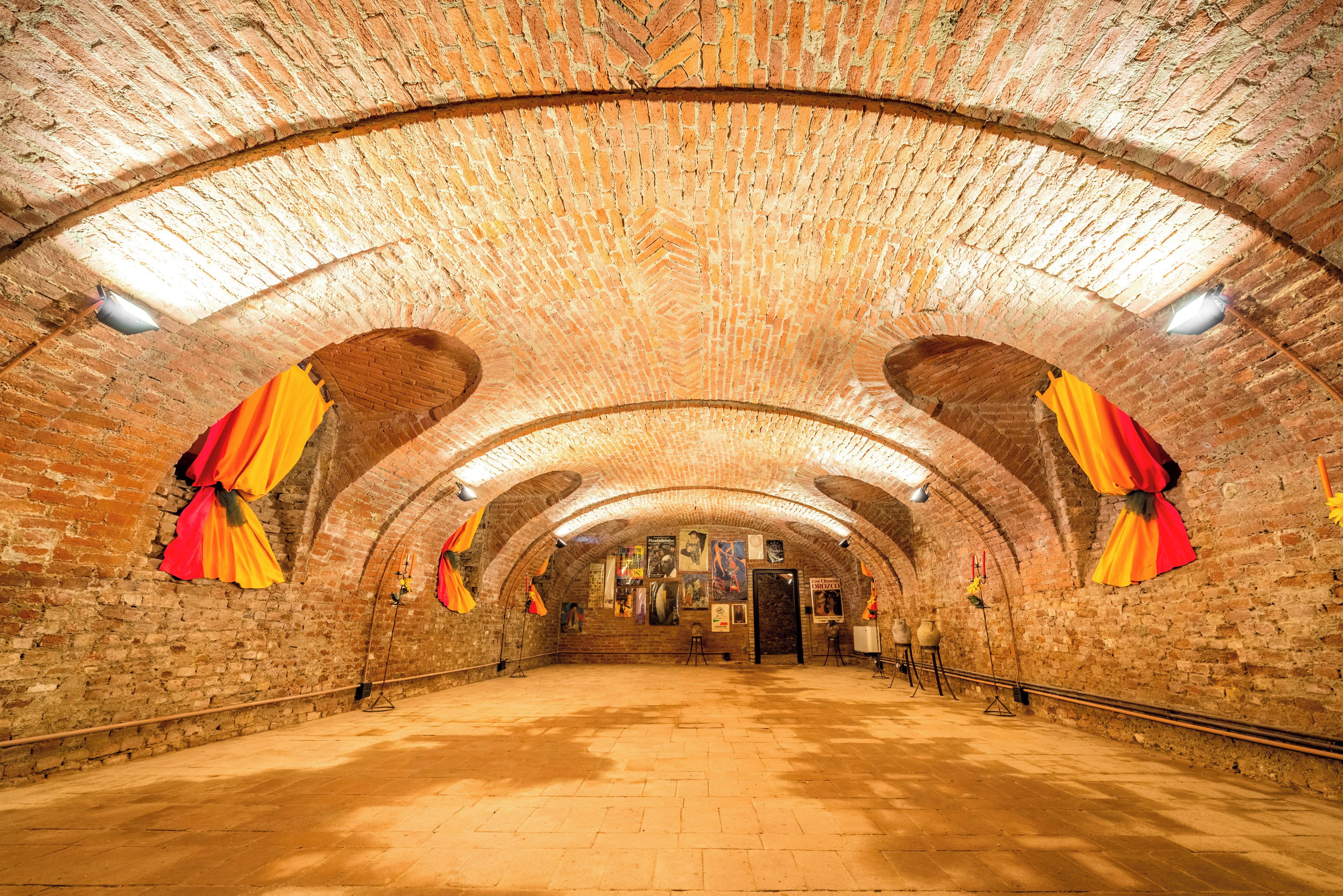 An arched brick tunnel with a vaulted ceiling, red and yellow drapes, and a central door.