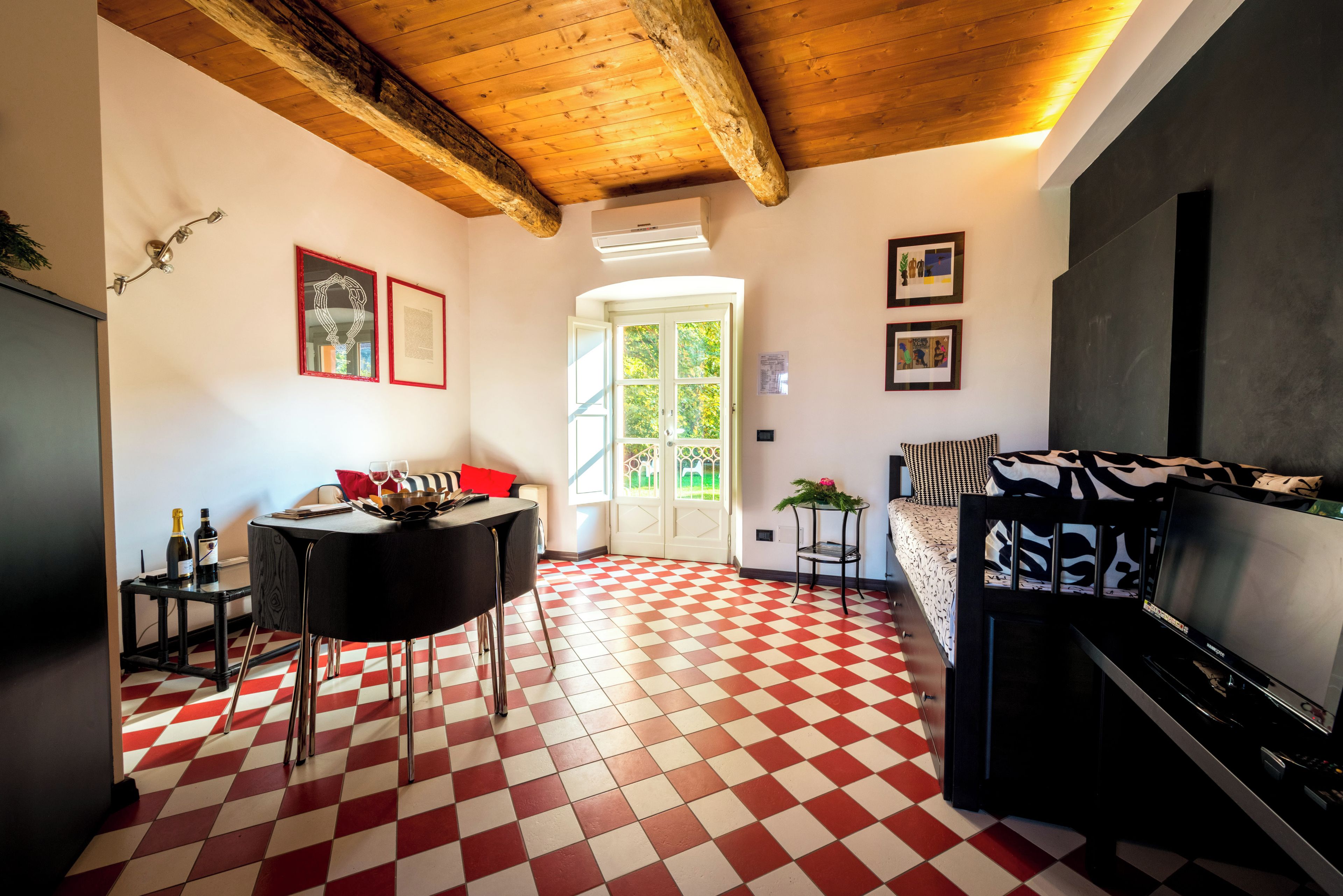 A room with a checkered floor, a dining table with chairs, a sofa, a television, and framed pictures on the wall.