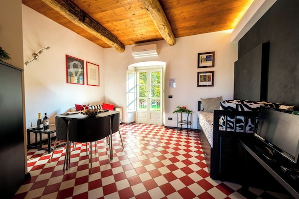 A room with a checkered floor, a dining table with chairs, a sofa, a television, and framed pictures on the wall. - Tenuta La Fiscala (Alessandria)