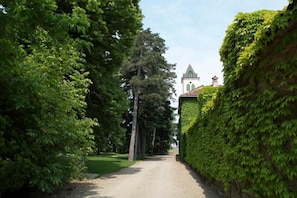 A pathway flanked by lush green hedges leading to a building with a pointed roof and arched windows. - Tenuta La Fiscala (Alessandria)