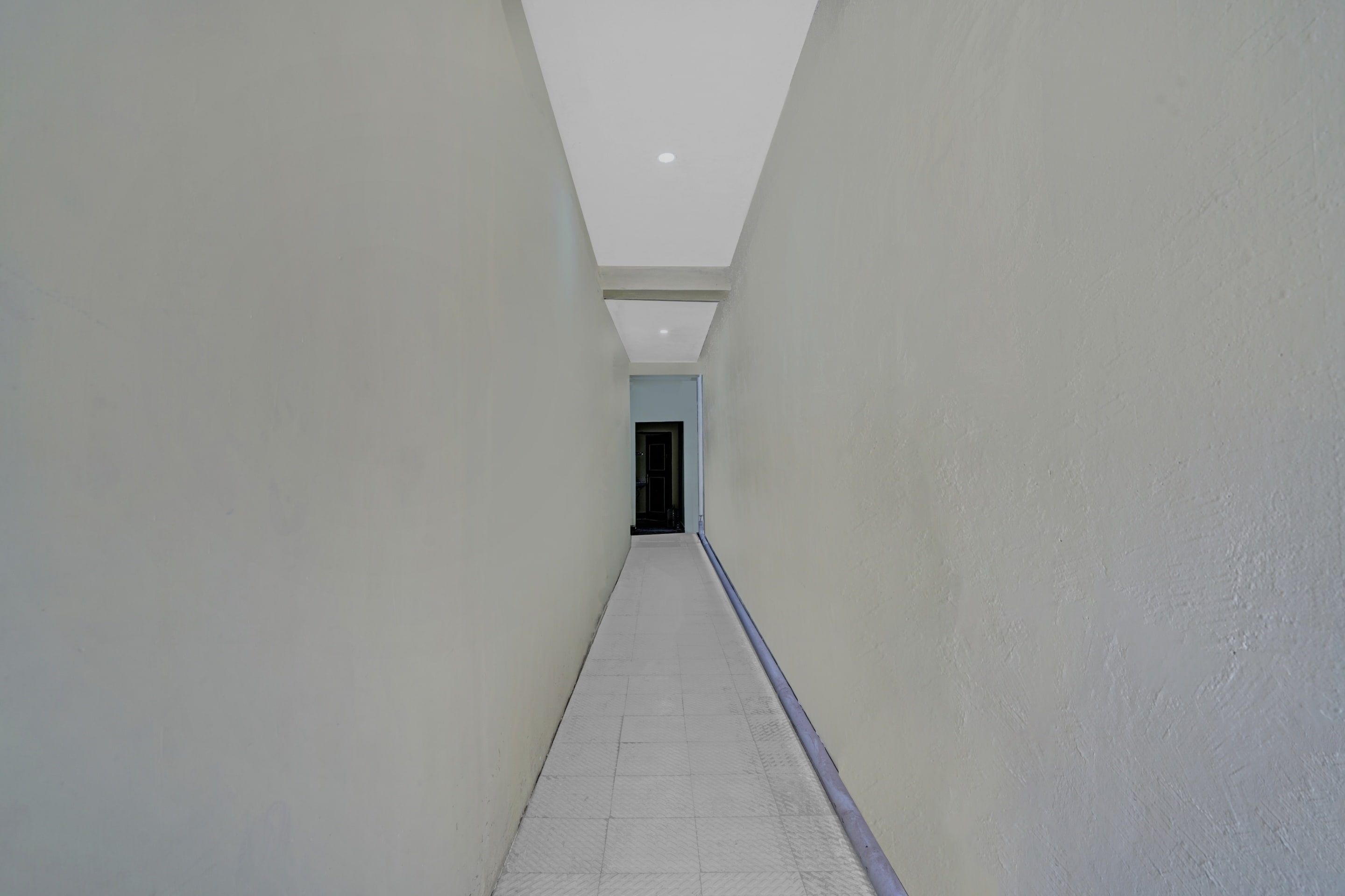 Un couloir aux murs blancs et au sol carrelé, qui mène à une porte.