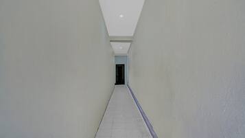 Un couloir aux murs blancs et au sol carrelé, qui mène à une porte.