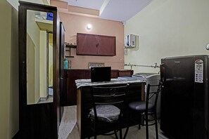 A compact room with a wooden cabinet, a small table with a chair, a refrigerator, and a water dispenser on the wall.