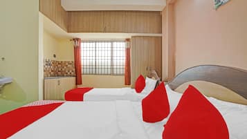 A hotel room with two beds, a window with curtains, a kitchenette, and a wooden ceiling.