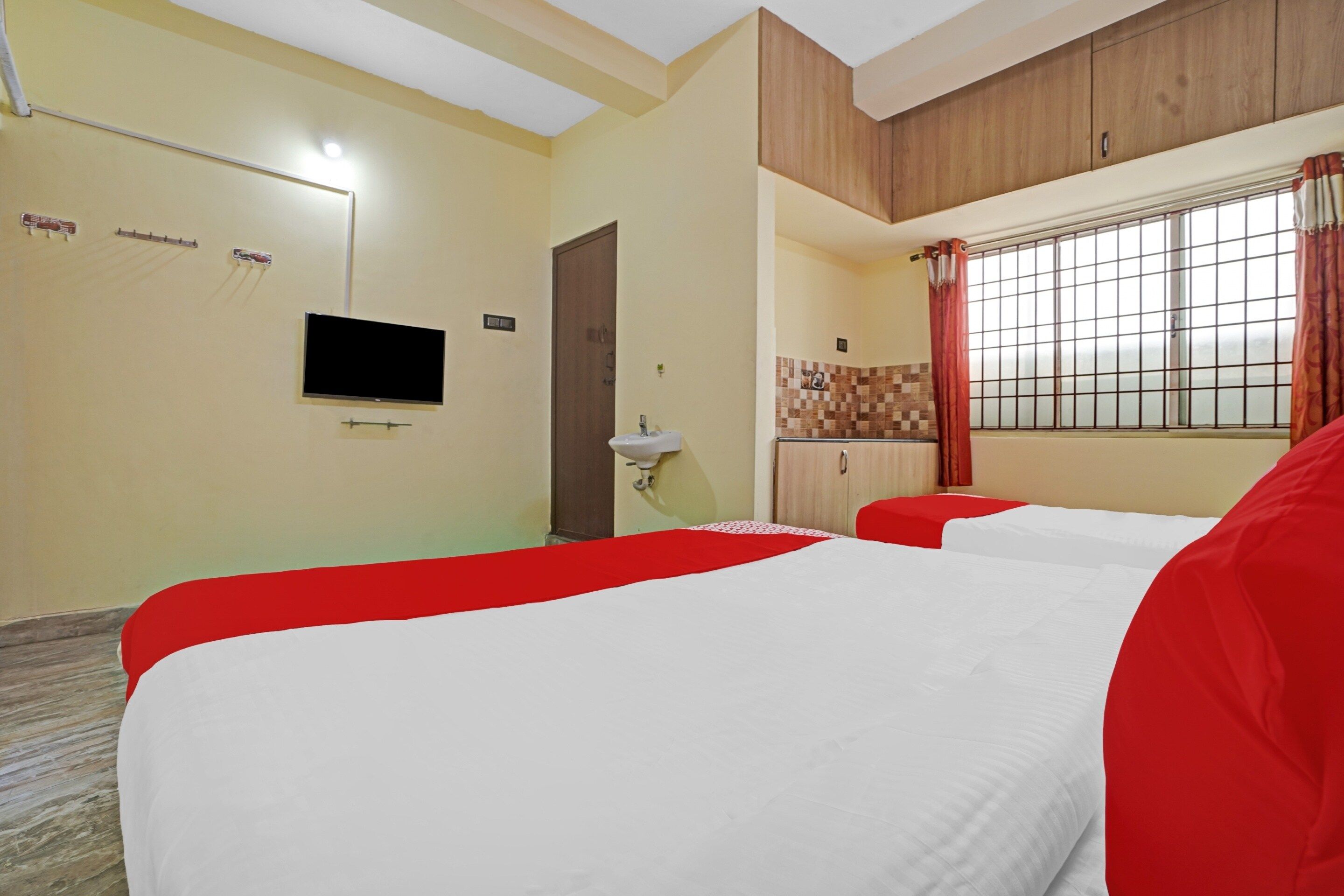 Une chambre d’hôtel avec deux lits, une télévision, un lavabo et une fenêtre avec des rideaux.