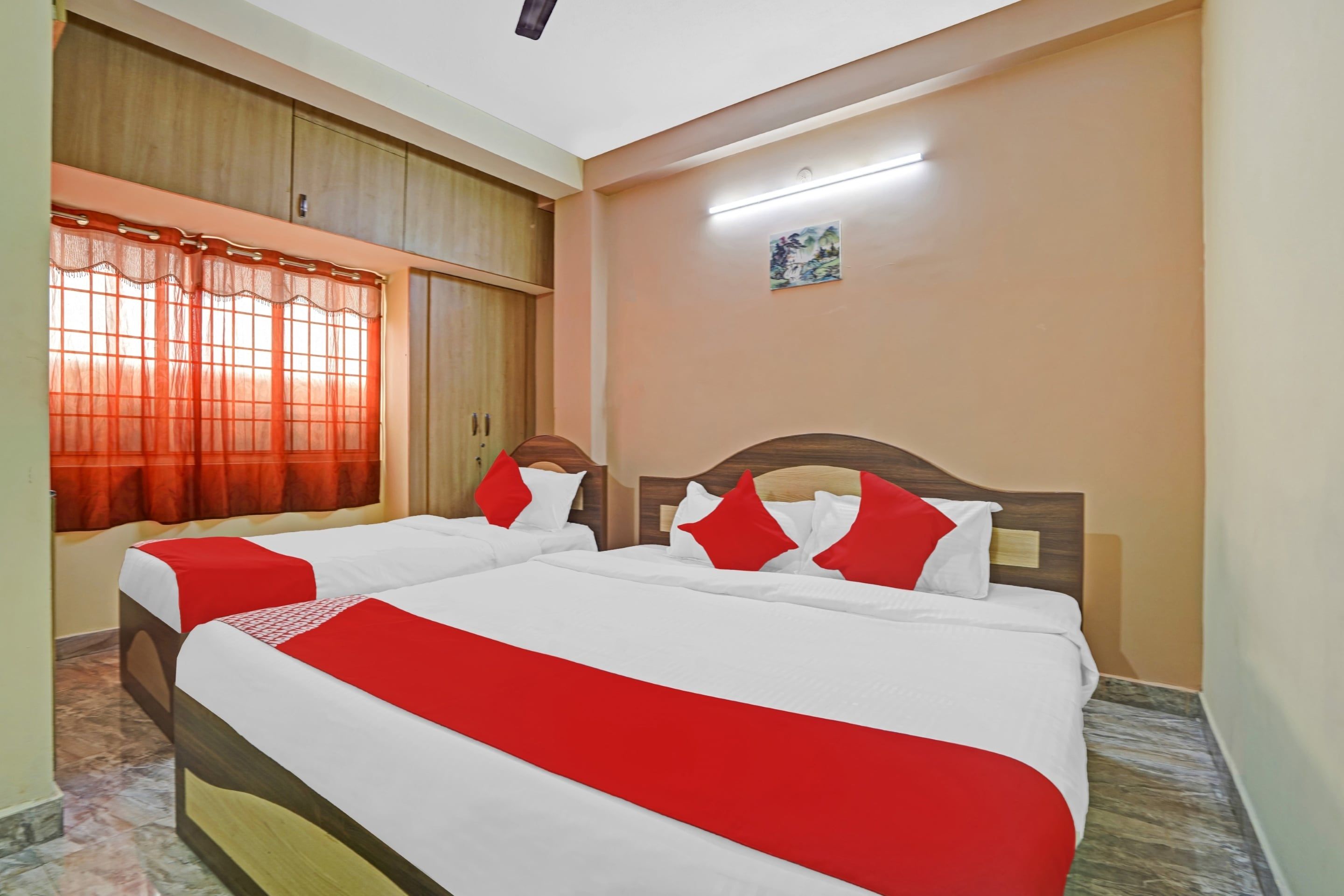 A hotel room with two beds, a window with curtains, a painting on the wall, and a ceiling light.