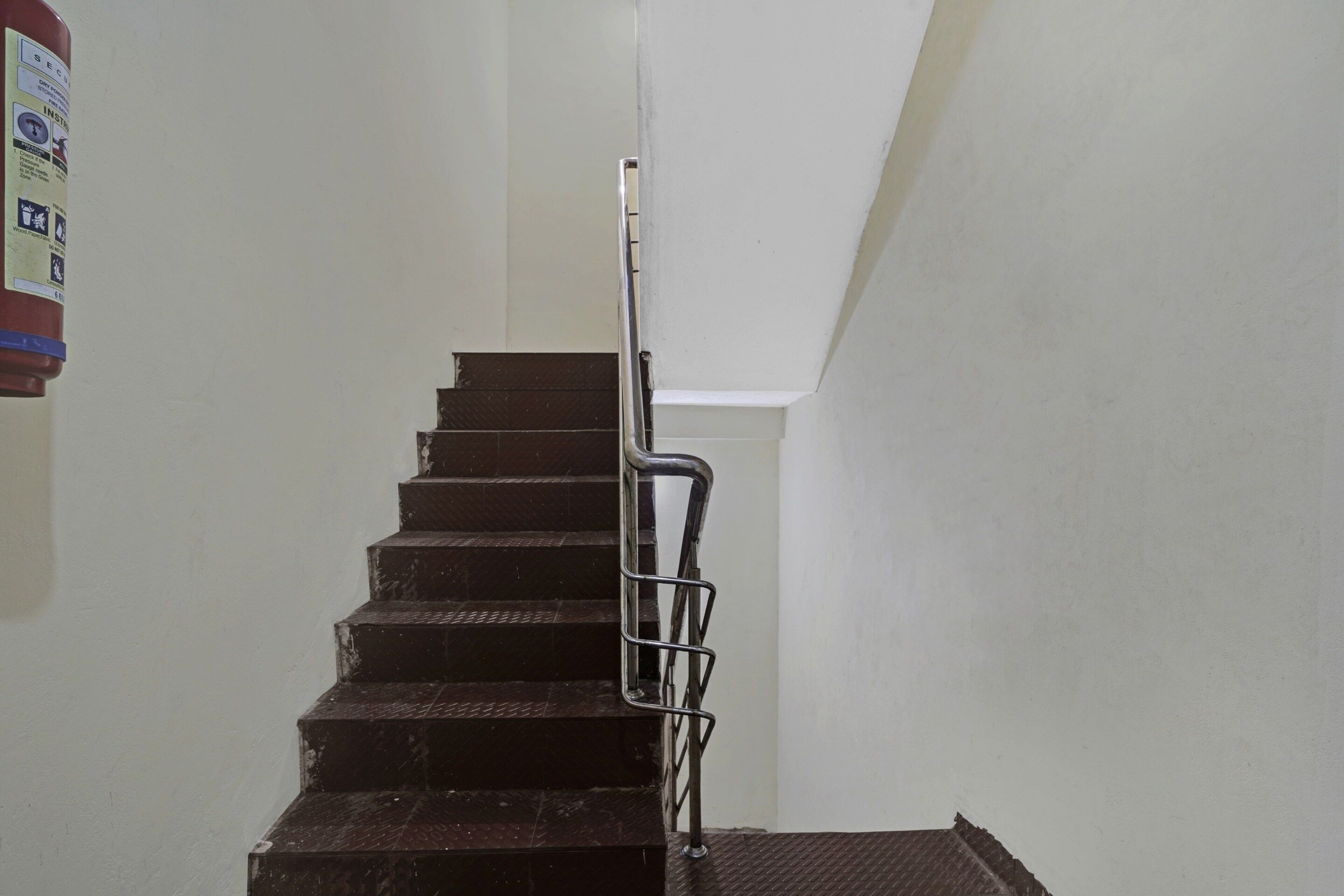 Un escalier doté d’une rampe métallique, menant à un palier avec un mur blanc.