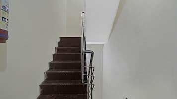 Un escalier doté d’une rampe métallique, menant à un palier avec un mur blanc.