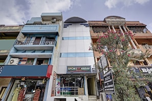 Un edificio de varios pisos con escaparate identificado como 'SPORTSCENTER' y cartel anunciando 'T.MAGAR RESIDENCY', ofreciendo habitaciones en alquiler diario y mensual.