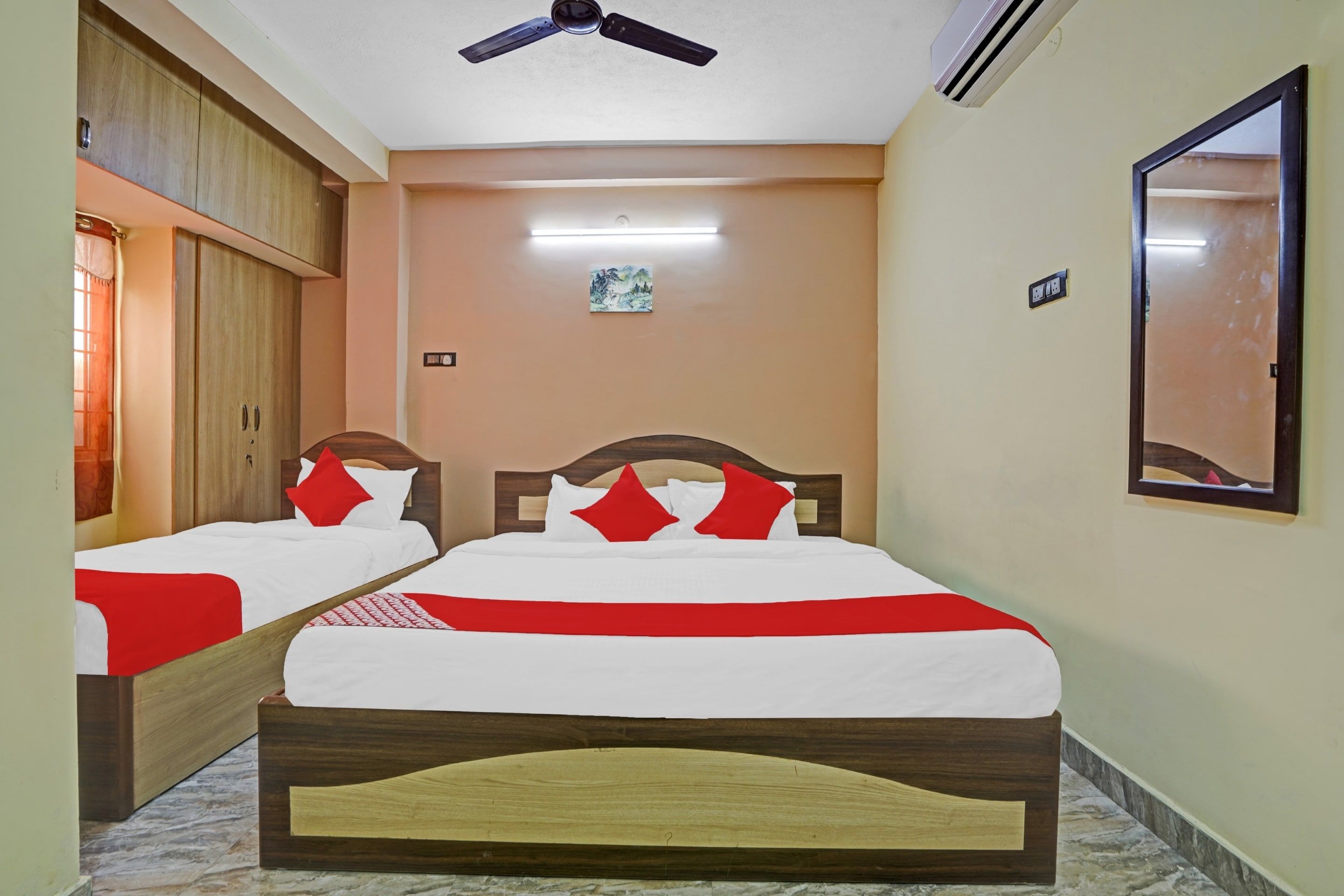 A hotel room with two beds, a ceiling fan, an air conditioning unit, a small painting on the wall, and a mirror.
