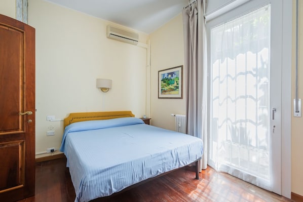 A bedroom with a bed, a wooden wardrobe, a radiator, and a window with curtains. - UR NEST Tullio Levi Civita - Prestigious 3 bedroom apartment in the first hills of Bologna (Bologna)