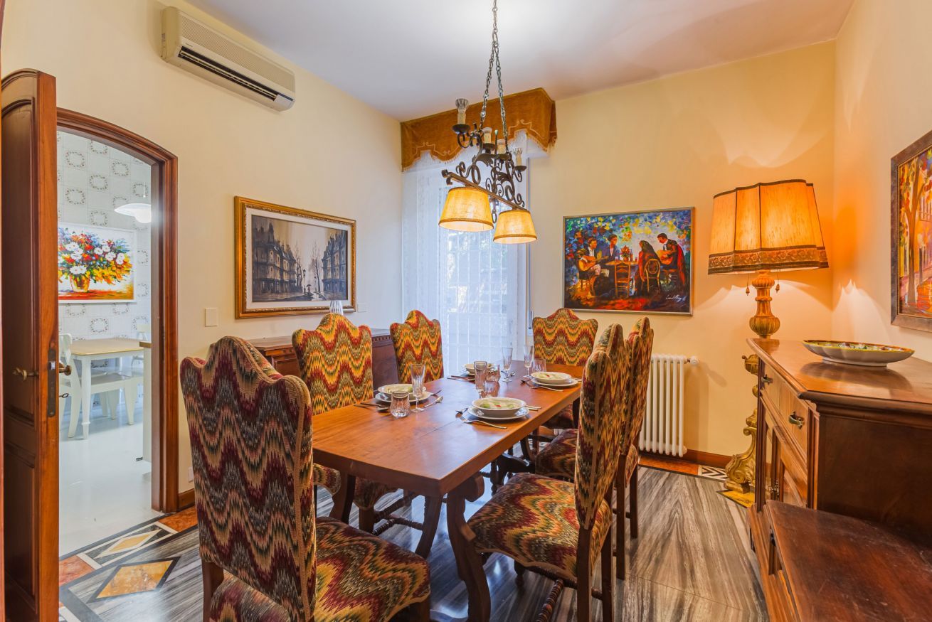 A dining area with a wooden table set for six, surrounded by patterned chairs, a chandelier, and artwork on the walls. - UR NEST Tullio Levi Civita - Prestigious 3 bedroom apartment in the first hills of Bologna (Bologna)