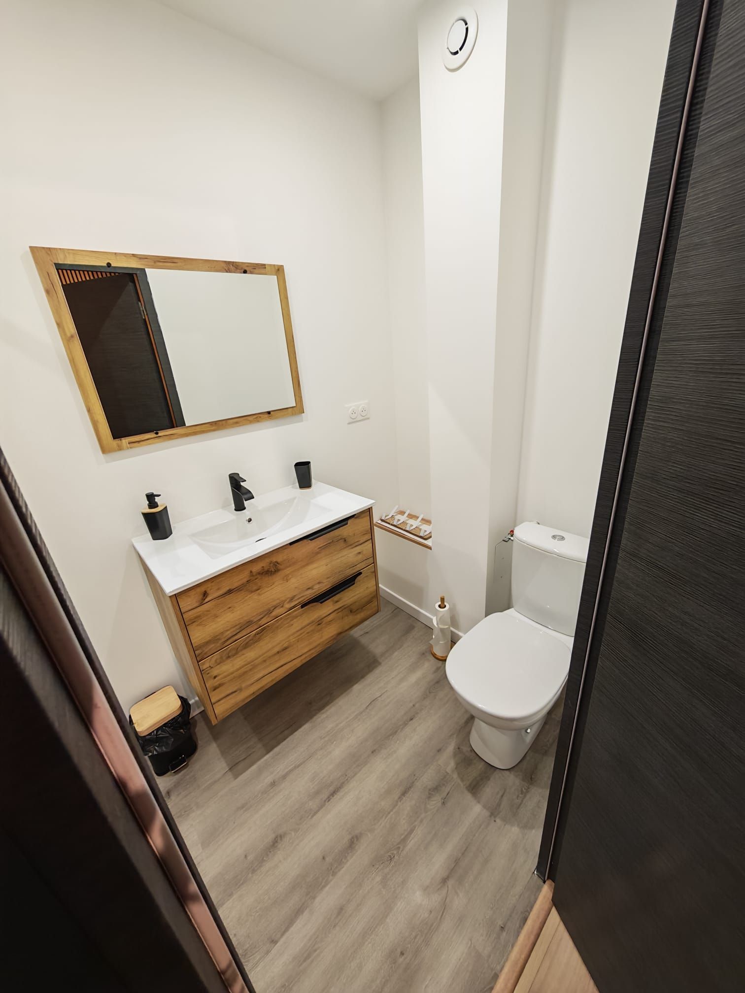 A bathroom with a wooden vanity, a white sink, a mirror, and a toilet.