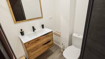 A bathroom with a wooden vanity, a white sink, a mirror, and a toilet.