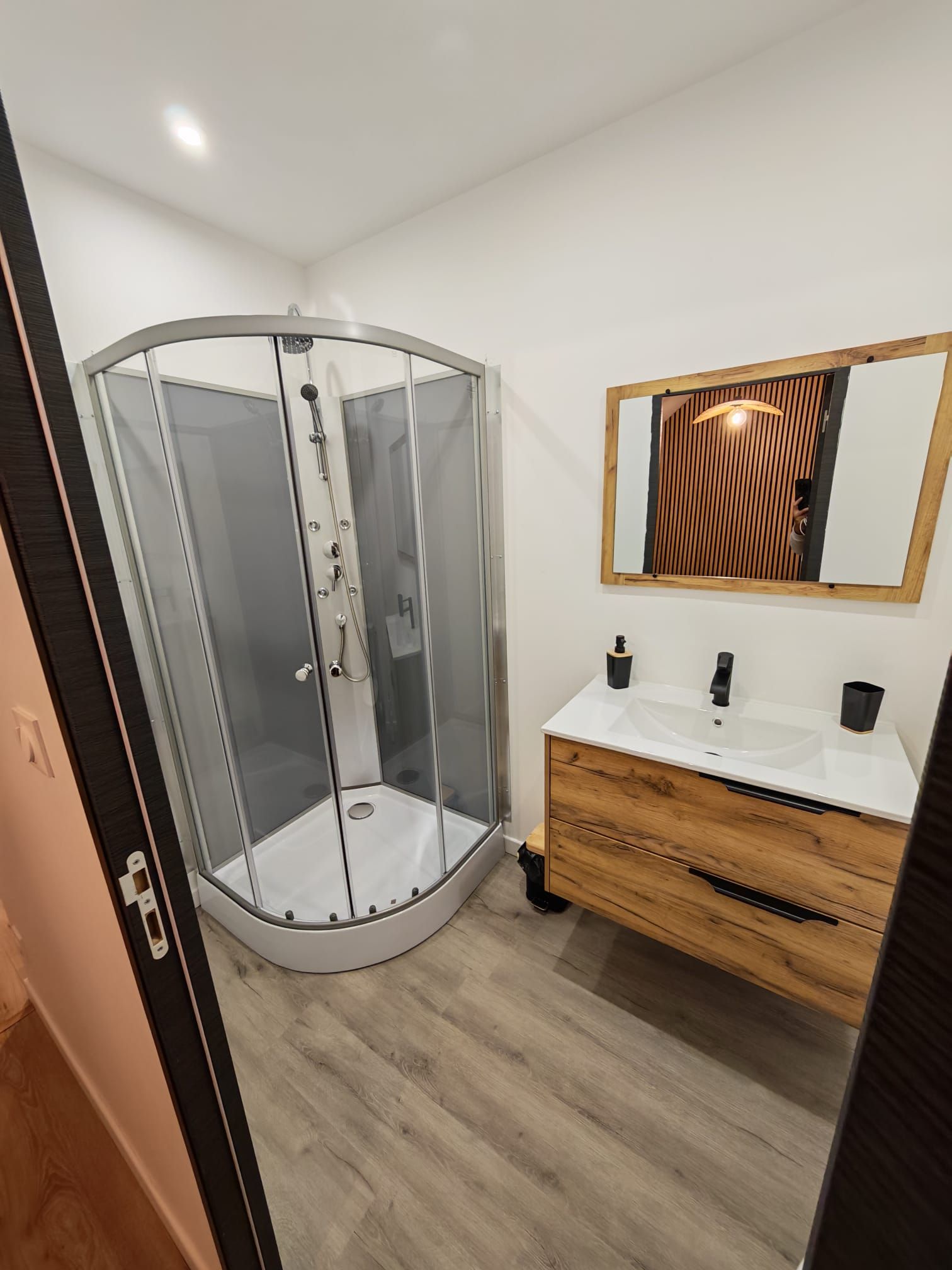 Ein modernes Badezimmer mit einer Duschkabine aus Glas, einem Holzausziehtisch und einem Spiegel mit Holzrahmen.