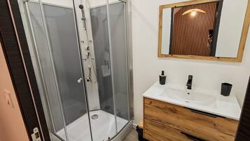 Ein modernes Badezimmer mit einer Duschkabine aus Glas, einem Holzausziehtisch und einem Spiegel mit Holzrahmen.