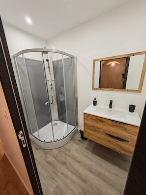 Ein modernes Badezimmer mit einer Duschkabine aus Glas, einem Holzausziehtisch und einem Spiegel mit Holzrahmen.