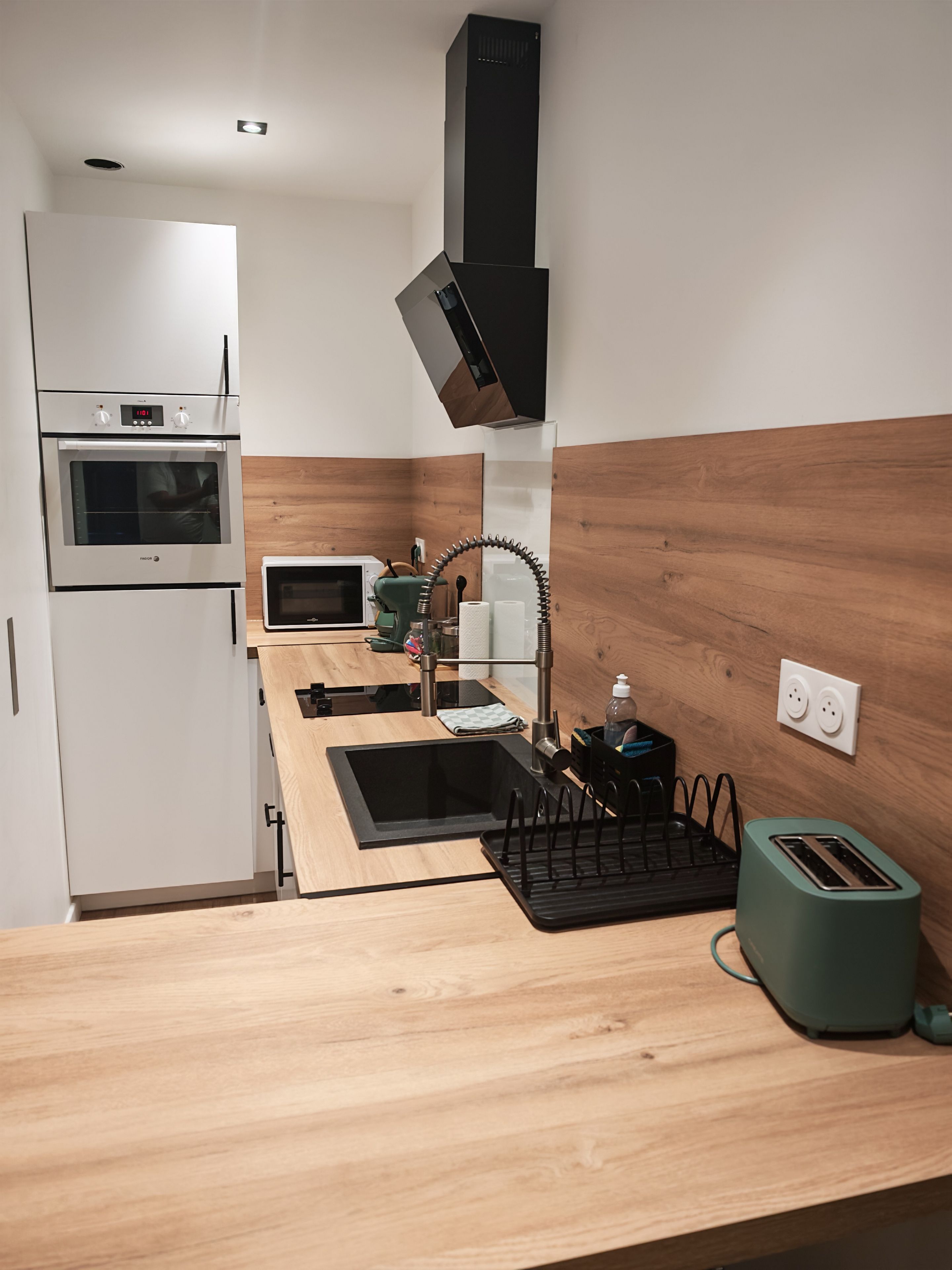 Ett kompakt kök med en inbyggd ugn, mikrovågsugn och en diskho med en modern blandare.