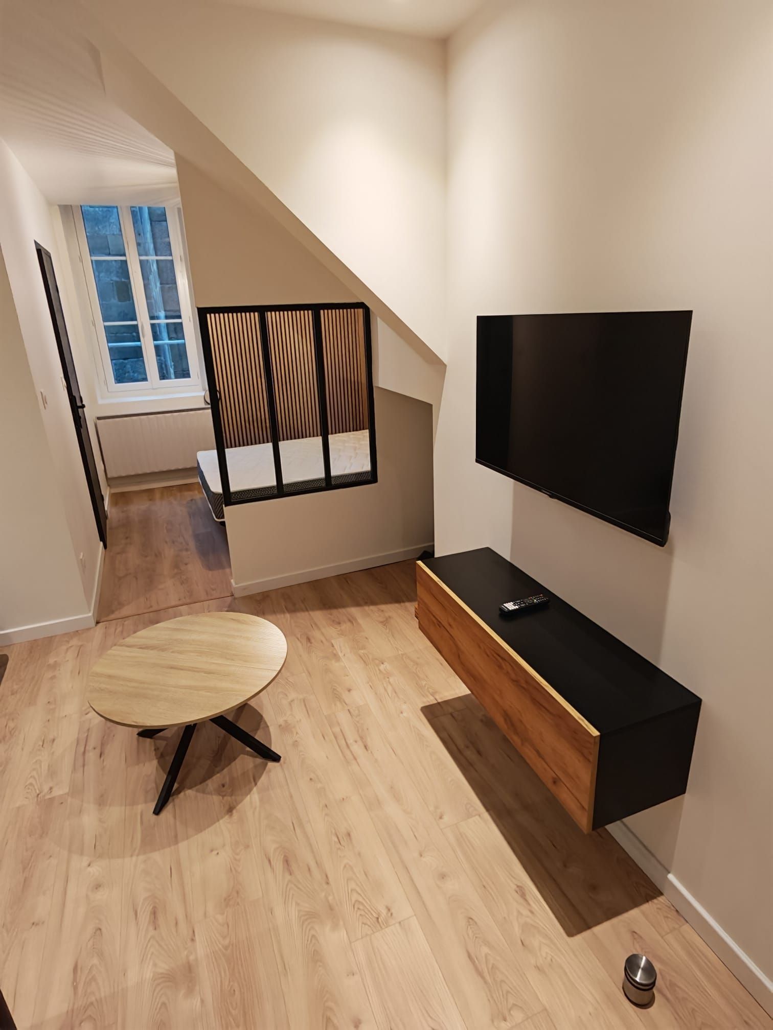Ett modernt vardagsrum med en platt-TV som är monterad på en svart vägg, ett matbord i trä och en trappa som leder upp till ett övre våningsplan.