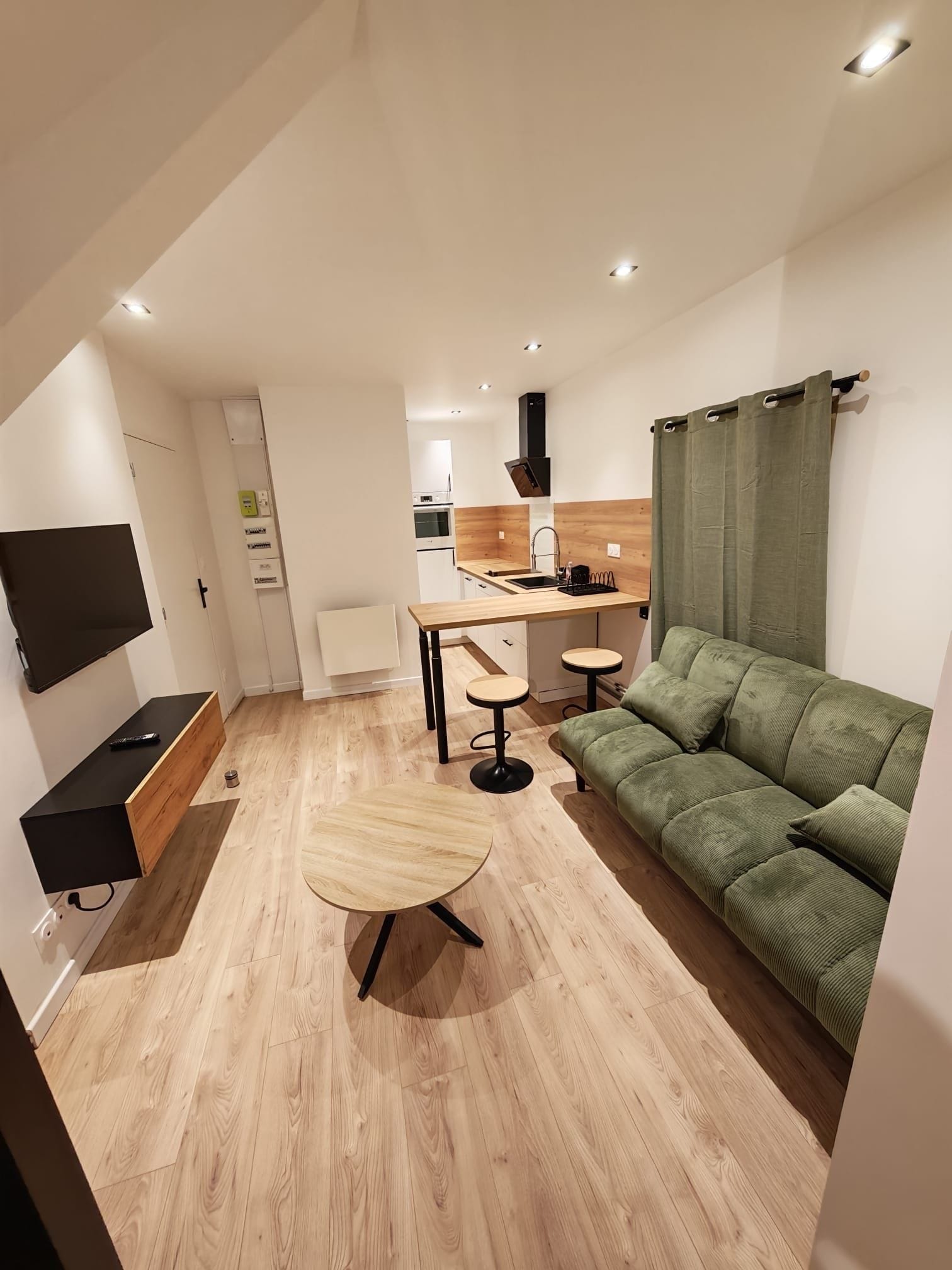 Ein modernes Wohnzimmer mit einem grünen Sofa, einem Holztisch und einem an der Wand befestigten Fernseher.