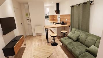 Ein modernes Wohnzimmer mit einem grünen Sofa, einem Holztisch und einem an der Wand befestigten Fernseher.