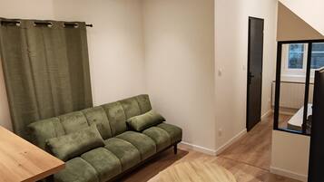 Ein kompakter Wohnraum mit einer Couch, einem runden Holztisch und einem Fenster mit Aussicht.