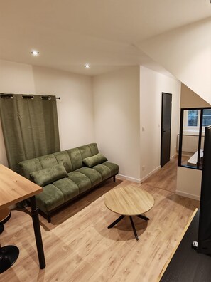 Ein kompakter Wohnraum mit einer Couch, einem runden Holztisch und einem Fenster mit Aussicht.