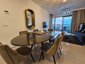A modern dining area with a round glass table, cushioned chairs, a large mirror, and a television. - Saviony view  (Jerusalem)