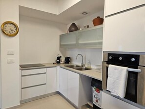 A modern kitchen with white cabinets, a stainless steel sink, a coffee maker, and an oven with a towel hanging on the handle. - Saviony view  (Jerusalem)