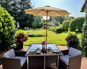 Ein Essbereich im Freien mit Tisch, Stühlen und Sonnenschirm.