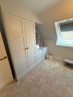 A room with a large white wardrobe, a small bench, and a window with blinds. - Beautifully Renovated 5-Bedroom Home with Garden & Parking (Epsom)