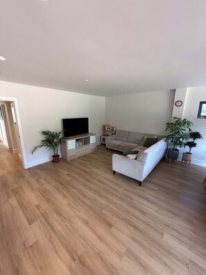 A spacious living area with a flat-screen TV, a sofa, and two potted plants. - Beautifully Renovated 5-Bedroom Home with Garden & Parking (Epsom)