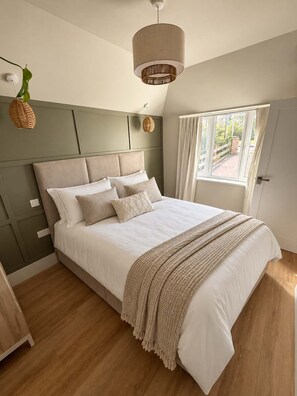 A bedroom with a bed, a hanging light fixture, a window with curtains, and a view of the outdoors. - Beautifully Renovated 5-Bedroom Home with Garden & Parking (Epsom)