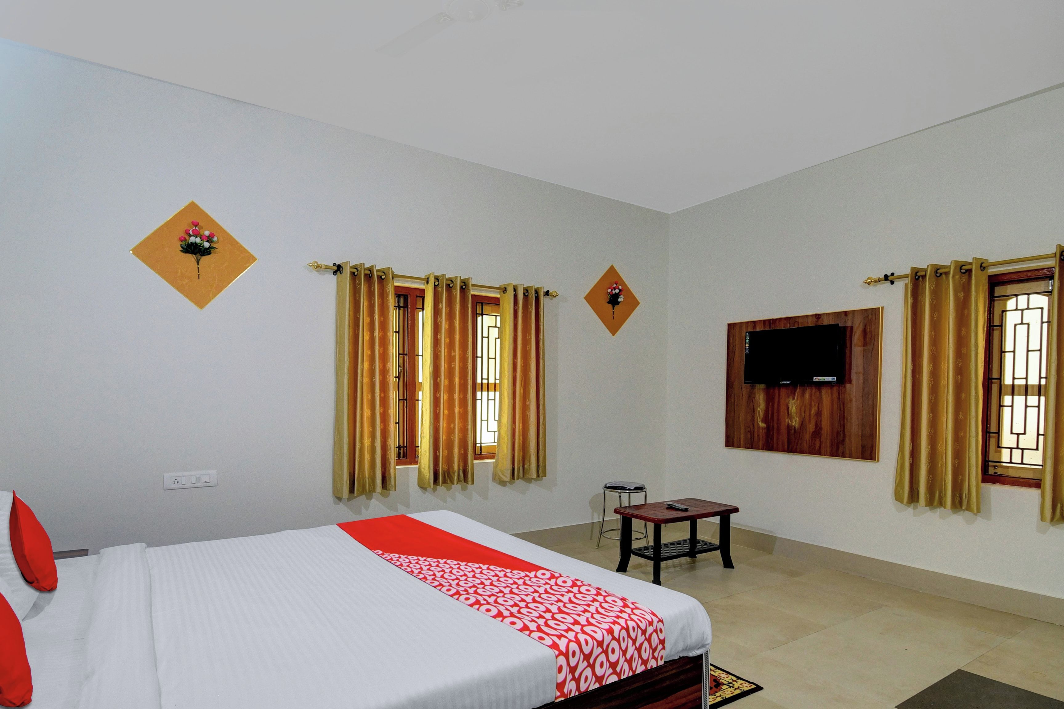 A hotel room with a bed, a TV mounted on the wall, and two windows with curtains.