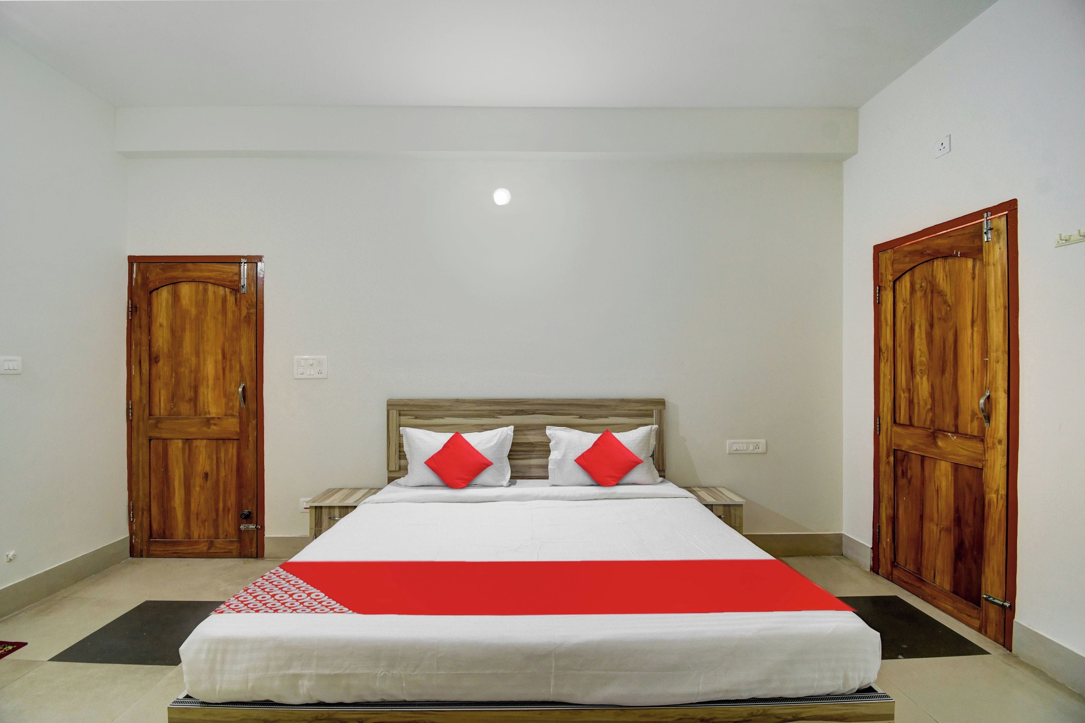 Uma cama de solteiro com cabeceira de madeira, duas almofadas brancas e uma almofada decorativa vermelha.