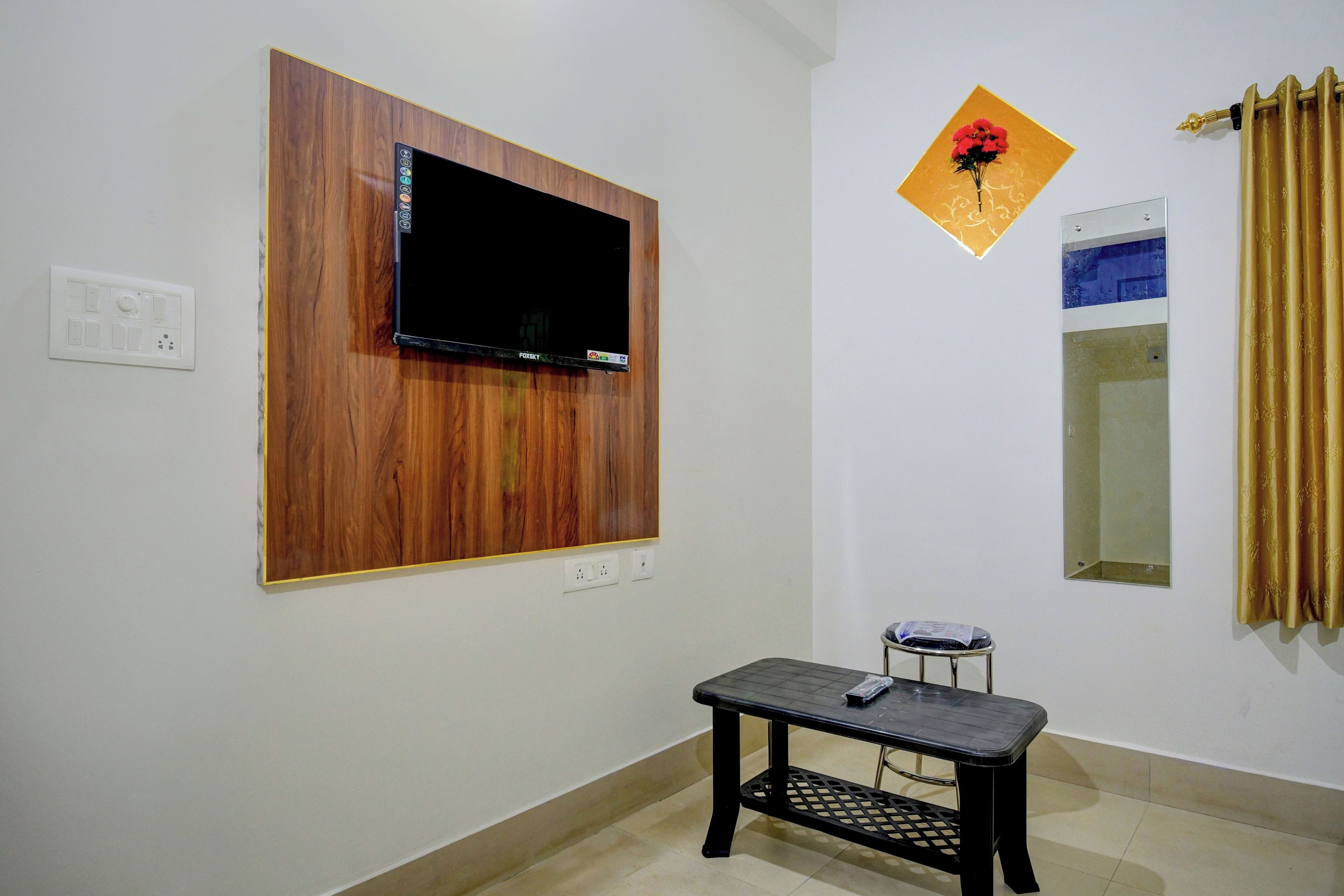 Una habitación con televisión montada, una mesita, un espejo y un adorno en la pared.