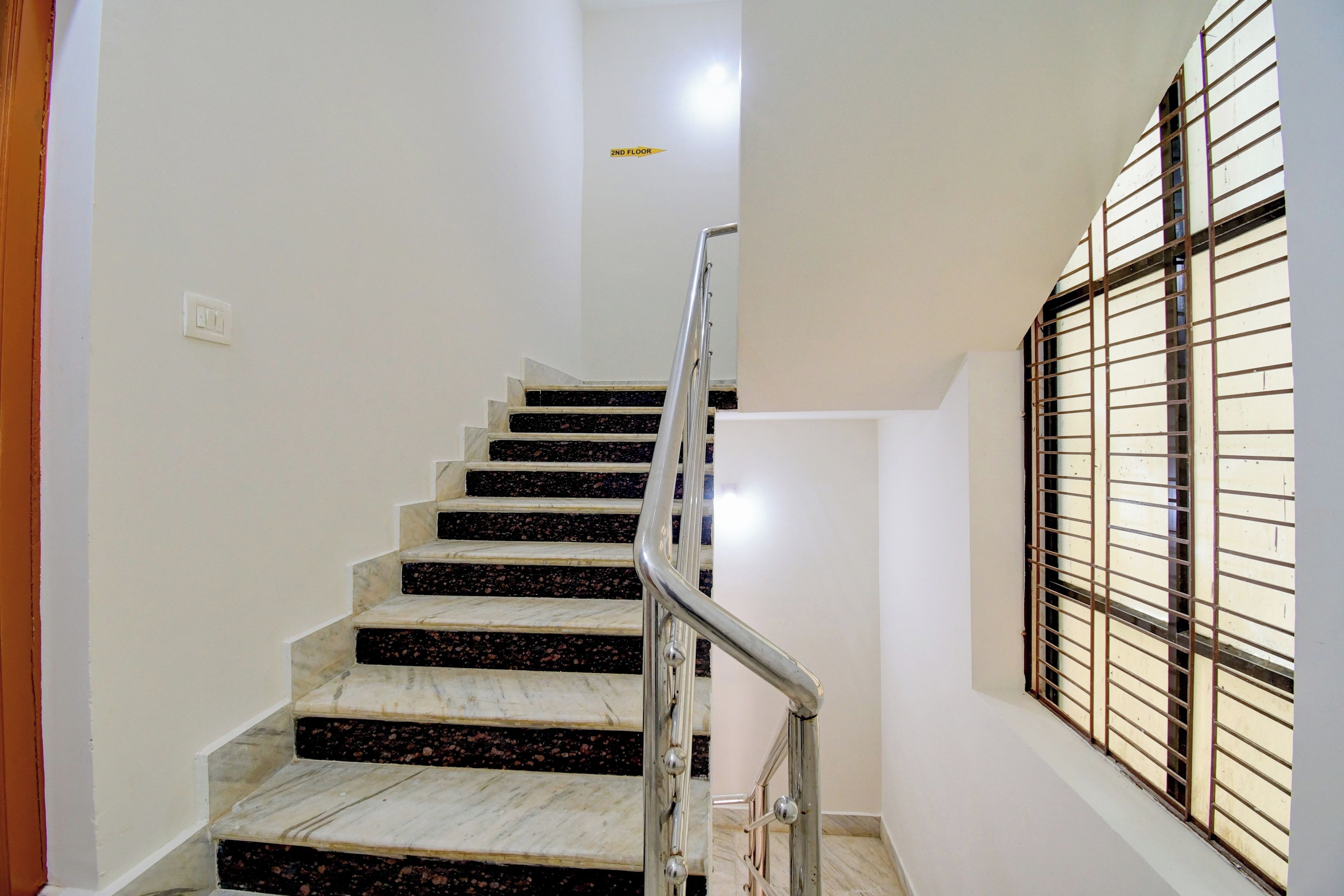 A staircase with marble steps leading to the 2nd floor, a metal handrail, and a window with metal bars on the right.