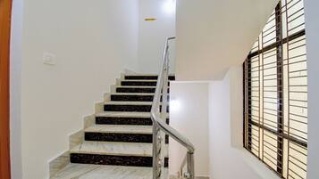 A staircase with marble steps leading to the 2nd floor, a metal handrail, and a window with metal bars on the right.