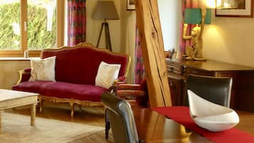 A room with a red sofa, a wooden dining table with a white bowl, a lamp, and a painting on the wall.