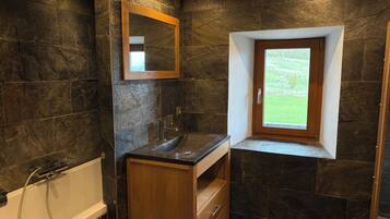 A bathroom with a bathtub, a wooden vanity, a mirror, and a window with a view of greenery.