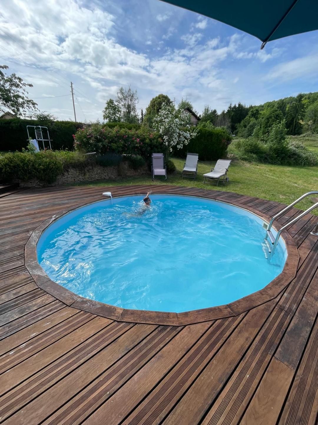 Una terraza circular de madera rodea una piscina donde una persona nada.