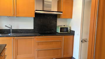 Cocina compacta con armarios de madera, campana extractora de acero inoxidable, microondas y pileta con grifo moderno.