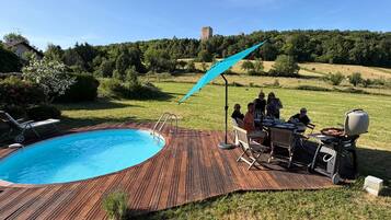 A poolside area with a wooden deck, a barbecue grill, and a group of people dining.