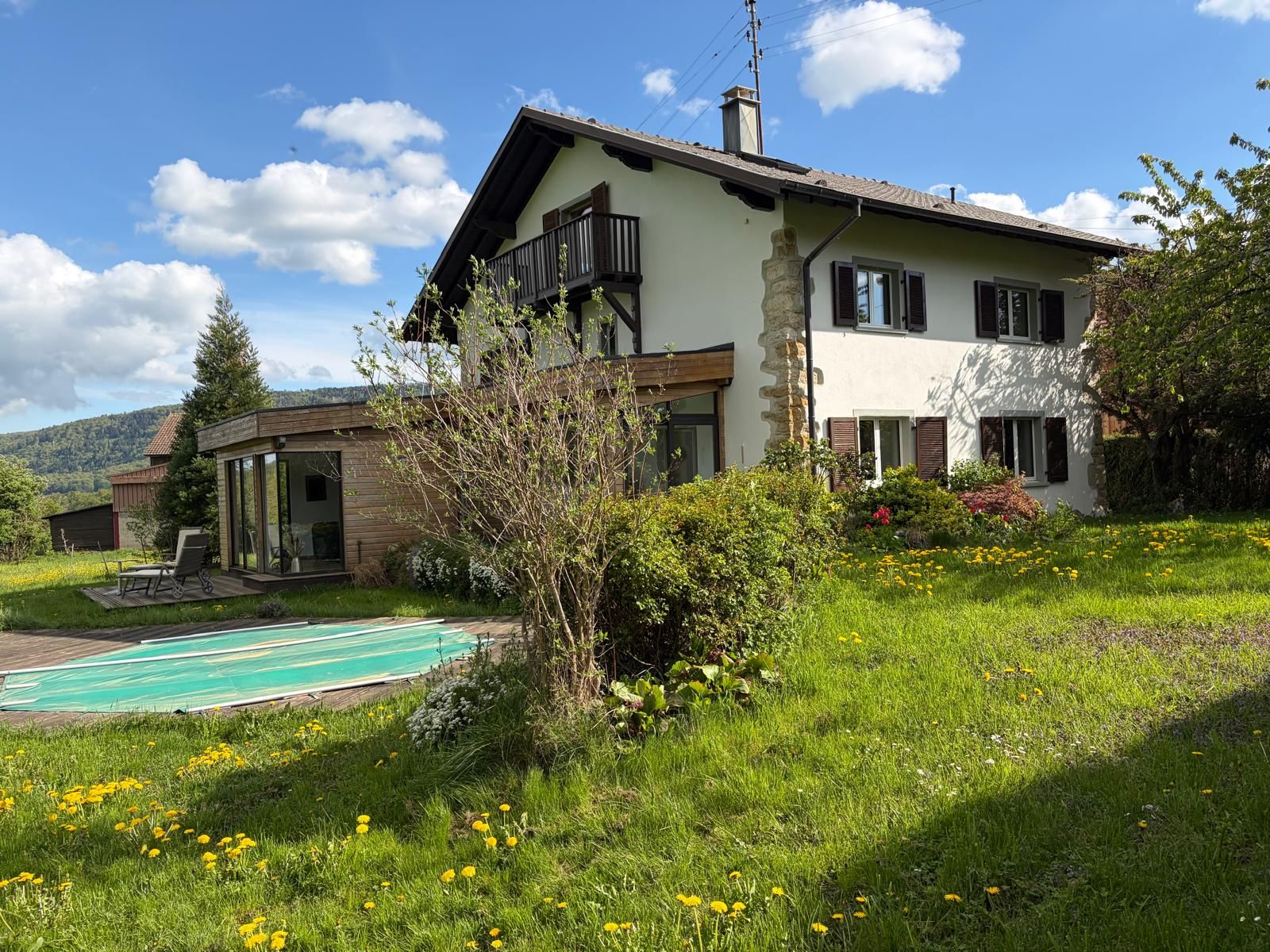A two-story house with a balcony, a swimming pool, and a garden with flowers.